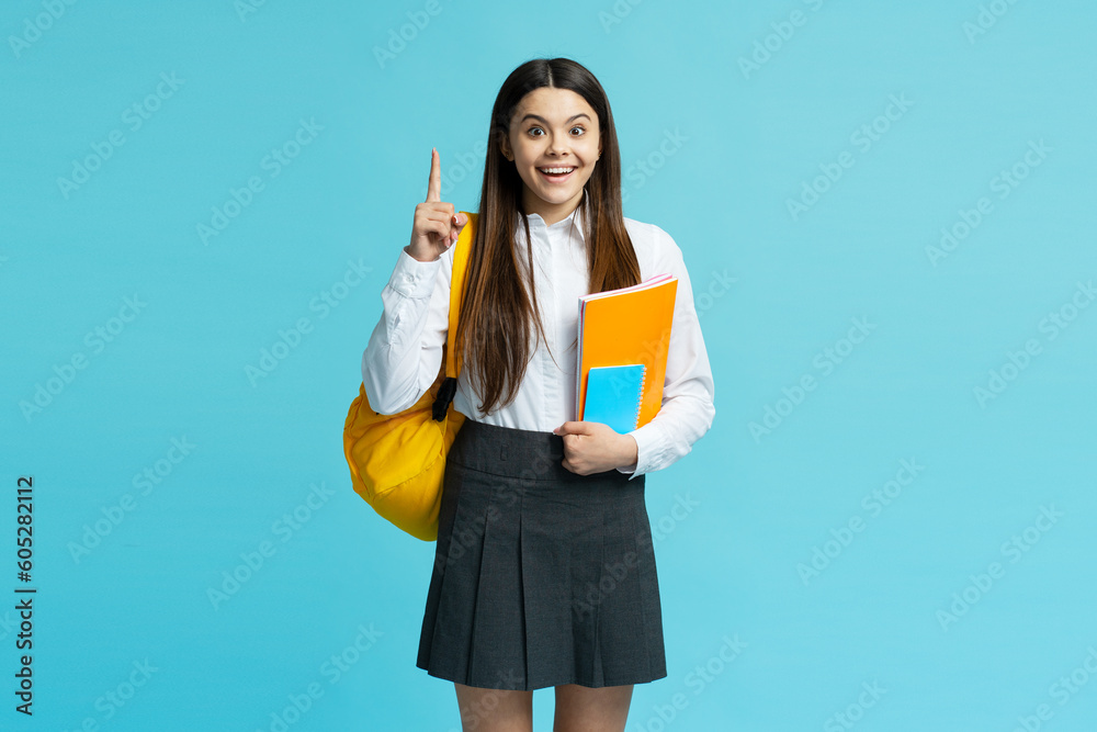 Portrait of smiling smart girl wearing school uniform, yellow backpack holding notebooks holding finder up, having idea isolated on blue background. Back to school, education concept Portrait of smiling smart girl wearing school uniform, yellow backpack holding notebooks holding finder up, having idea isolated on blue background. Back to school, education concept