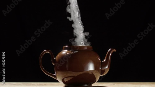 Hot steam rise from brown teapot as boiling water is poured inside, close slomo photo