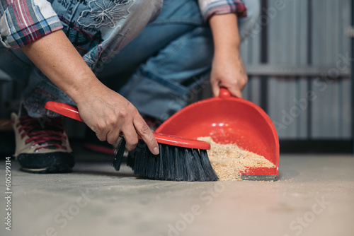 Hands picking up sawdust residues with a broom and dustpan after wood working