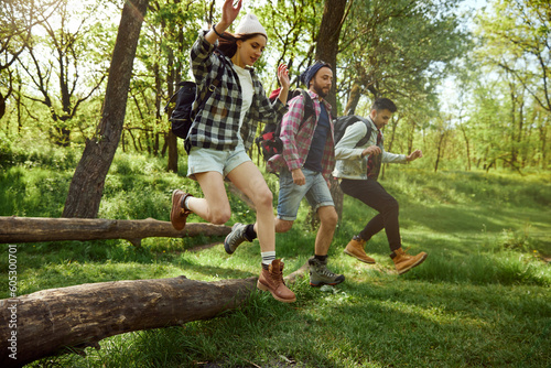 Group of young people, friends walking in forest, going hiking on warm sunny day, jumping over big tree. Having fun outdoors. Concept of active lifestyle, nature, sport and hobby, friendship © master1305