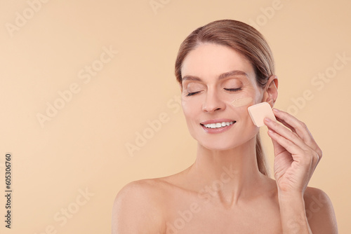 Woman blending foundation on face with makeup sponge against beige background. Space for text