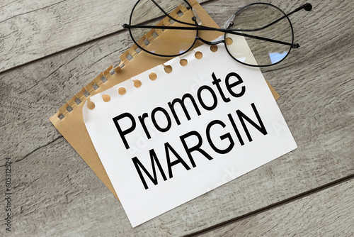 PROMOTE MARGIN text. on torn paper near glasses on a light wooden background.