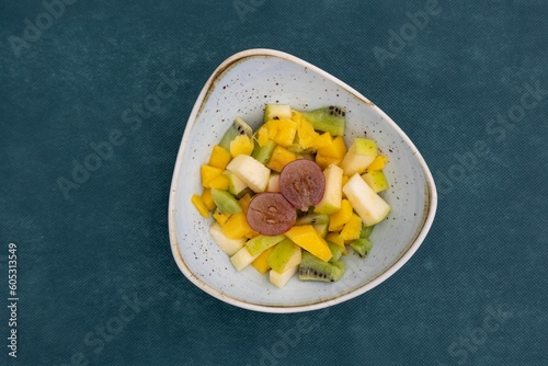 Top view of bright juicy and delicious fruit salad in a plate against green background