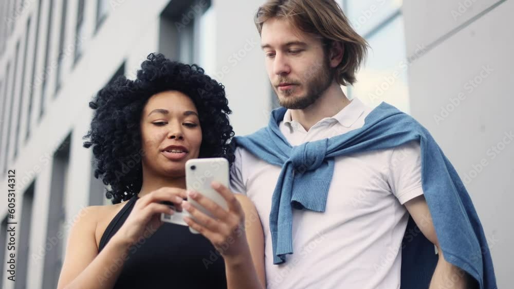 Cute young interracial couple paying with credit card on smartphone together at city Happy customers with shopping bags doing payments online in internet store outdoors Cute young interracial couple paying with credit card on smartphone together at city Happy customers with shopping bags doing payments online in internet store outdoors