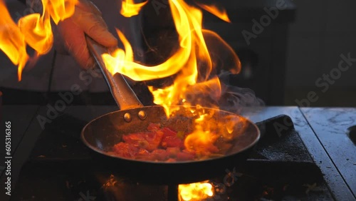 Detail view on flaming skillet in hand of professional chef. Male cook mixing and frying vegetables cooking tasty flambe style dish for visitors of restaurant. Concept of cooking. Slow mo Front view