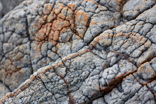 Rocks on a beach of Martinique island in the Caribbean sea. Grey and reddish volcanic or limestone rock with diagonal cracks, gaps and fissures weathered by sea water surf. Rough surface background.