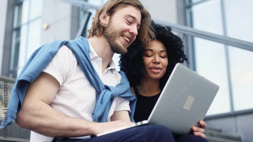 Smiling young interracial couple looking at laptop computer screen choose products in online internet store make order online booking or plan trip at city Happy people enjoying time together outdoors Smiling young interracial couple looking at laptop computer screen choose products in online internet store make order online booking or plan trip at city Happy people enjoying time together outdoors