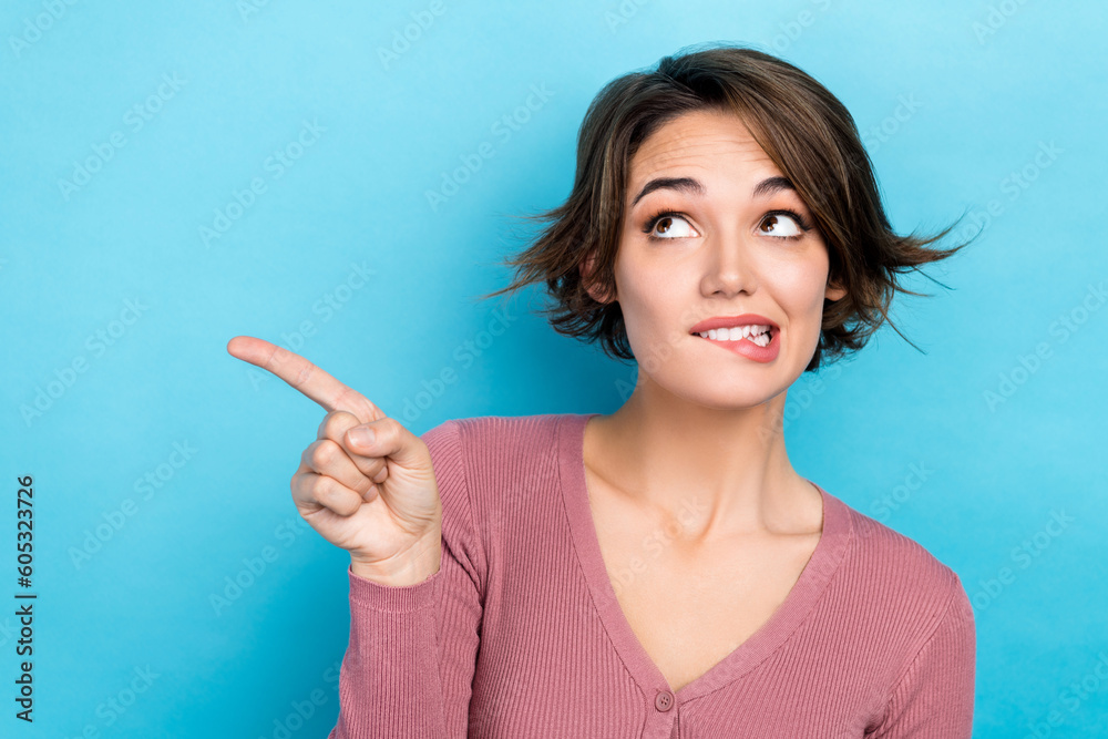 Photo of funny interested lady direct index finger look empty space bite lips wear pink shirt isolated blue color background Photo of funny interested lady direct index finger look empty space bite lips wear pink shirt isolated blue color background