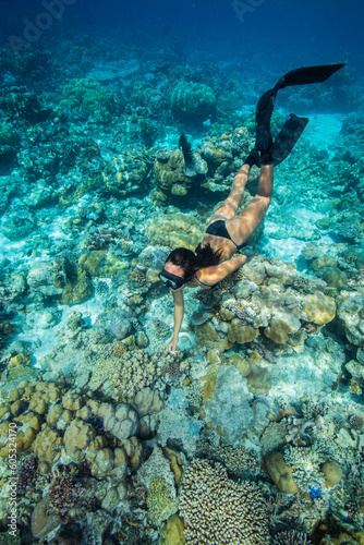 A young woman in bikini free dives above a coral reef in clear tropical water 