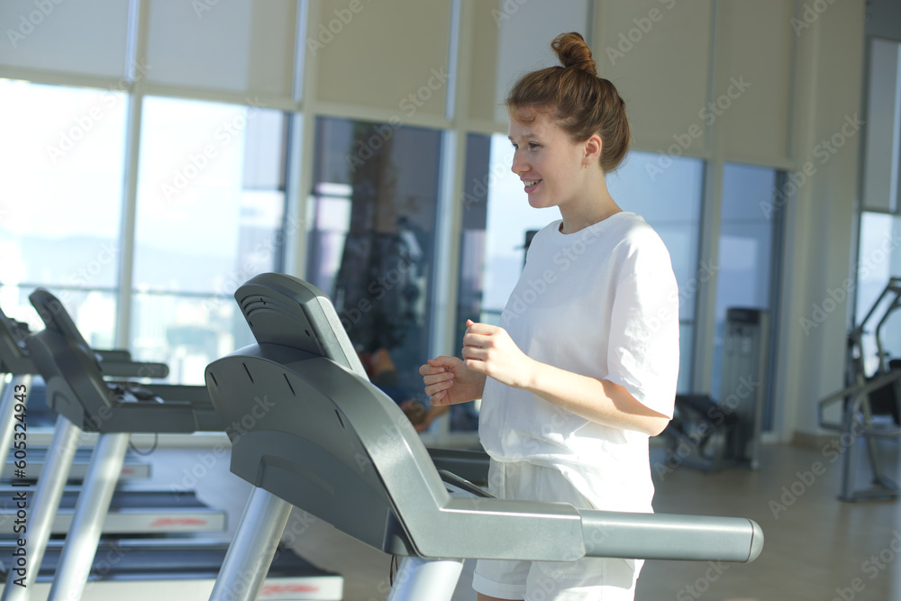 Happy young fit woman training in the gym, running jogging on treadmill, doing cardio exercise and smile. Healthy lifestyle, sport, fitness concept