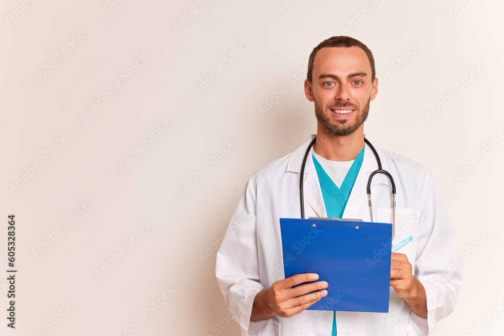 Young bearded smiling doctor holding tablet folder in his hands, posing in white medical coat against white background, copy space, professional people concept