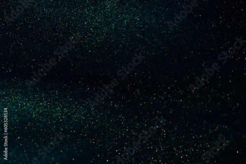 Abstract strains of gold particles in a green liquid. A dark mysterious glistening fluid background. Golden glittering particles on dark green-blue background.