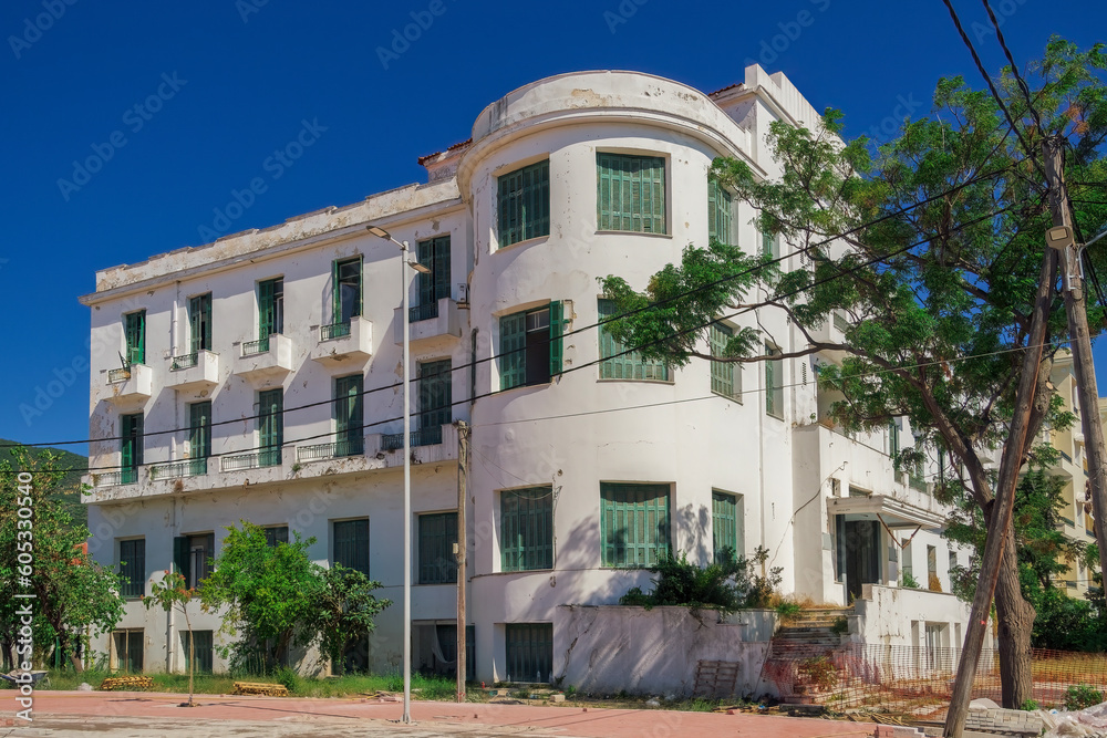 A low-rise deserted 1930s hotel with a decayed facade and green wooden window shutters under the summer blue sky.