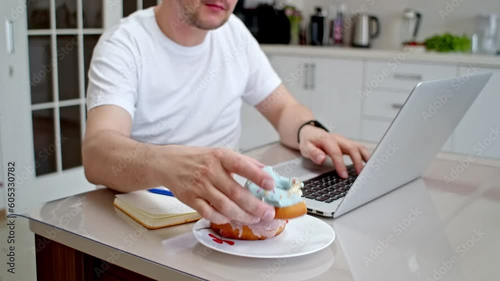 Freelancer man eating unhealthy junk food while working from home. Attractive handsome young male feeling happy and enjoy, use laptop computer study learn online and eat donut in the kitchen Freelancer man eating unhealthy junk food while working from home. Attractive handsome young male feeling happy and enjoy, use laptop computer study learn online and eat donut in the kitchen