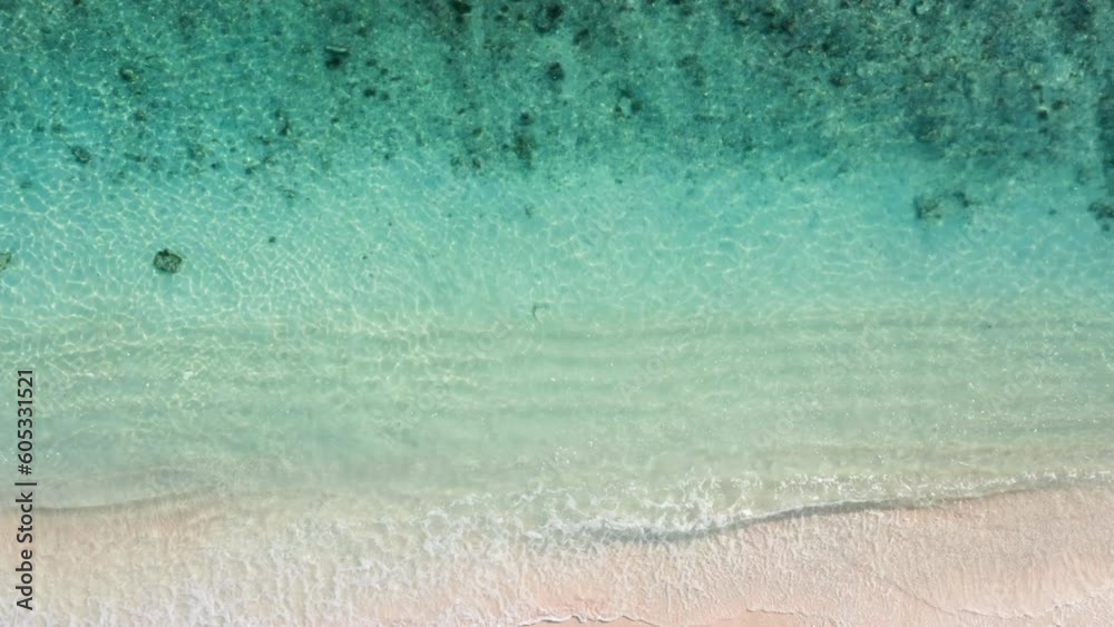 Beautiful ocean water ripples rolling on white sand beach. Aerial footage of transparent sea waves with caustic and pink sand in tropical paradise. Drone view of exotic island in tropics. Serenity. 
