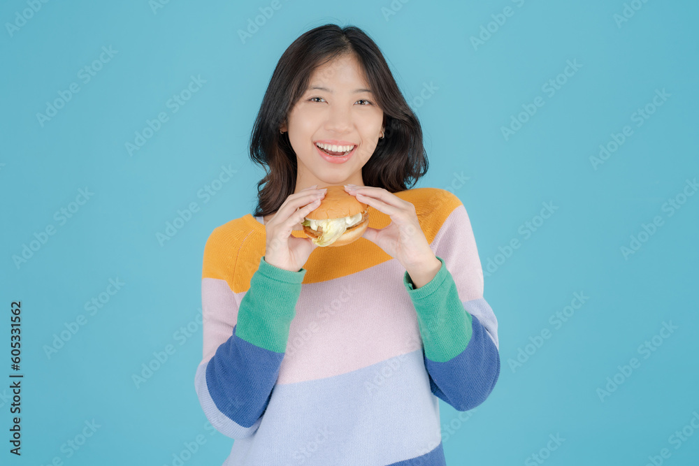 Beautiful young woman smiling happily while holding burger in her hand Beautiful young woman smiling happily while holding burger in her hand