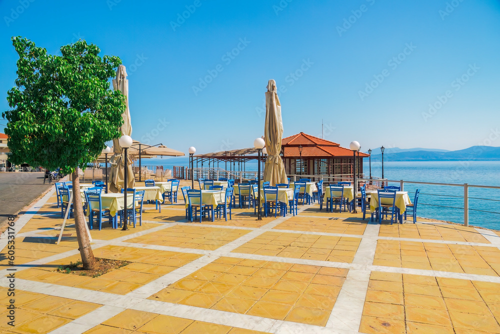 Empty tavern restaurant by the seafront with wooden chairs and tables under a bright sun in summer.