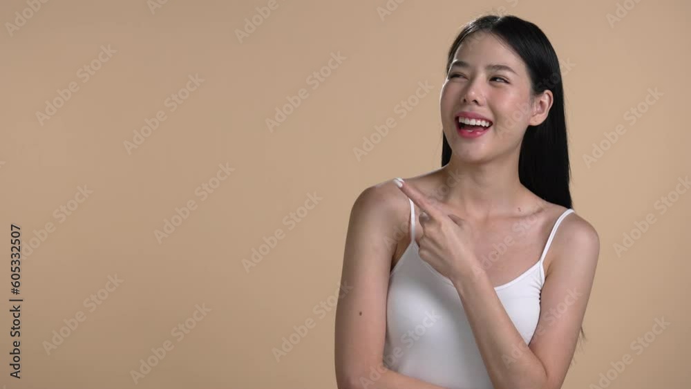 Attractive young Asian woman pointing at copy space at beige background Attractive young Asian woman pointing at copy space at beige background