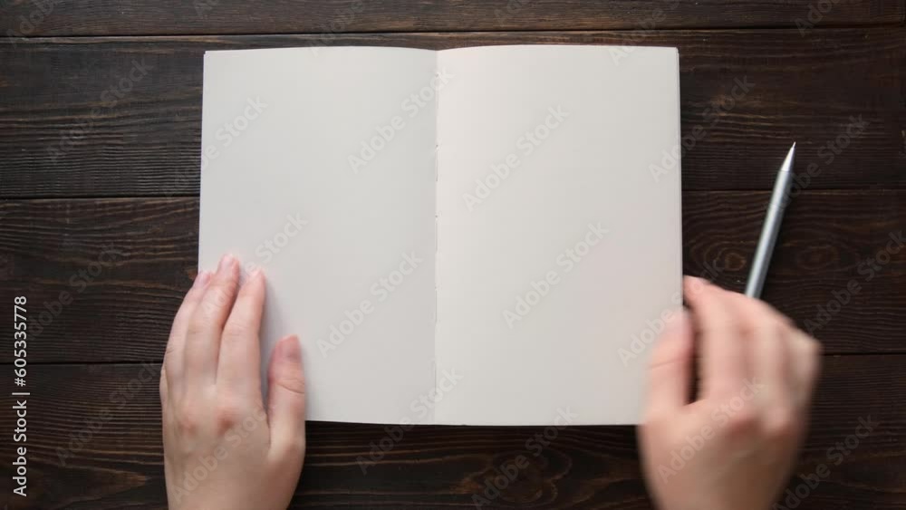 Hand opens clean note and start writing on a brown wooden background. 4K footage top view