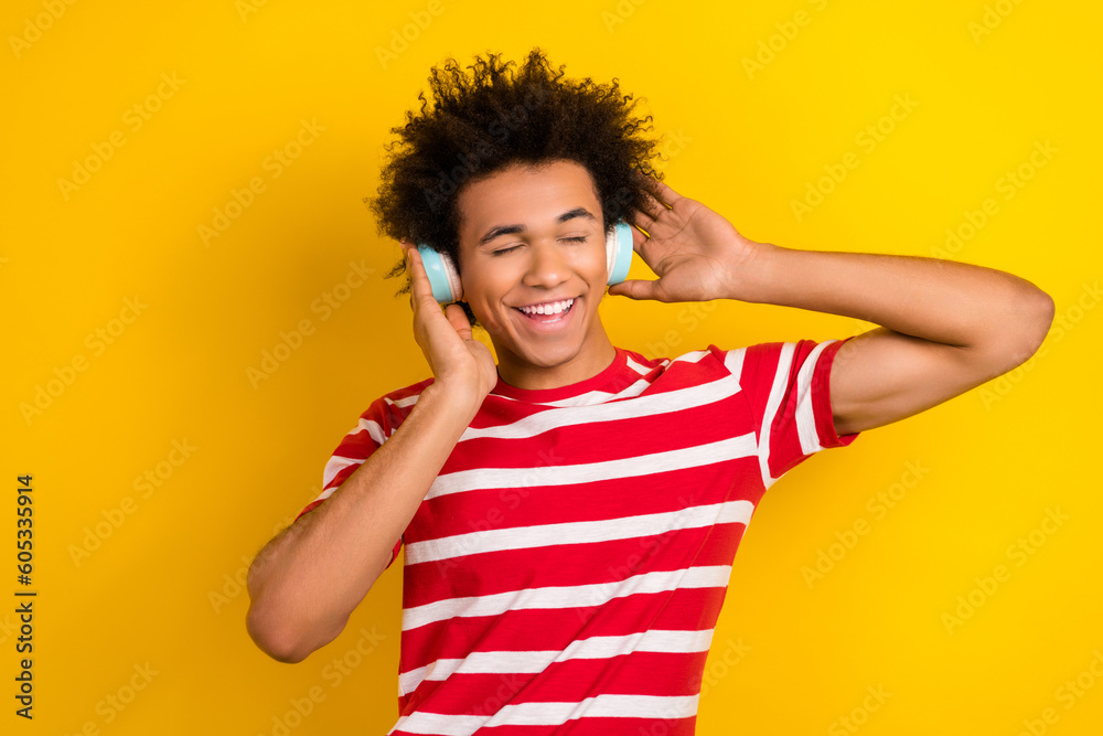 Photo of excited dreamy guy dressed red t-shirt listening songs earphones isolated yellow color background Photo of excited dreamy guy dressed red t-shirt listening songs earphones isolated yellow color background
