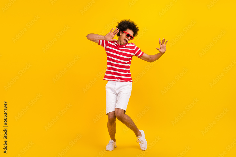 Full length photo of funky cool man wear striped t-shirt dark spectacles having fun dancing isolated yellow color background