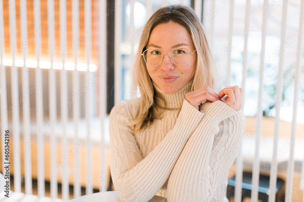 Portrait of comforting happy cozy woman in glasses in knitted winter white warm sweater in cafe Portrait of comforting happy cozy woman in glasses in knitted winter white warm sweater in cafe