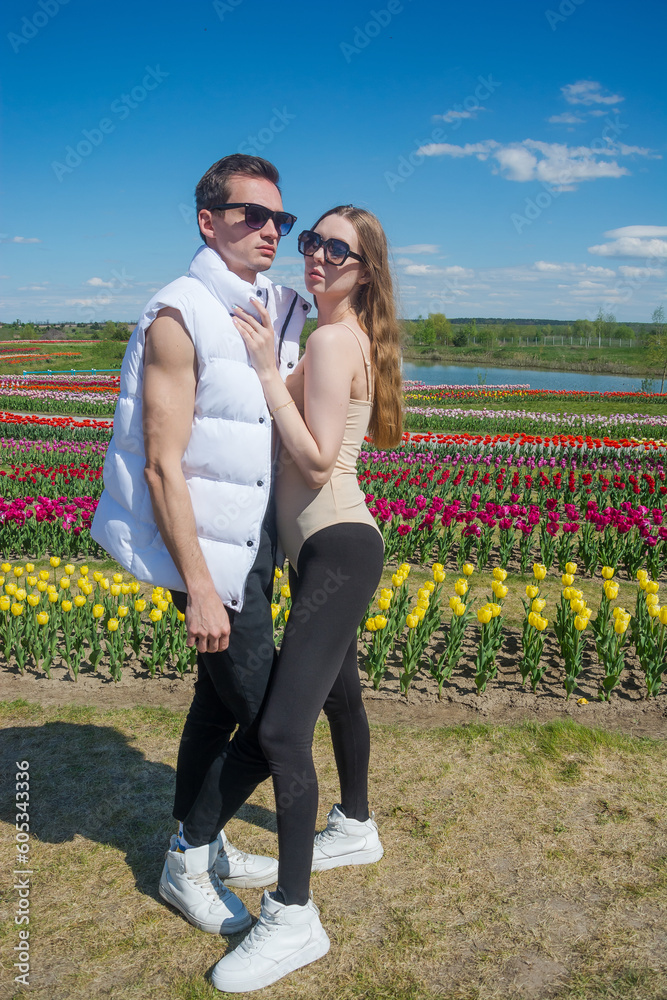 Young beautiful smiling couple in sports clothes, on the background of a field of colorful tulips.