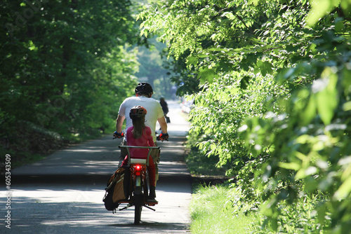 Father riding bike carrying daughter seated on the back on the bikeway