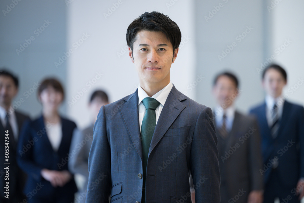 若い社長や社員のイメージ 逆光の中カッコいいスーツの男性の正面のアップ 背景にビジネスマン 若い社長や社員のイメージ 逆光の中カッコいいスーツの男性の正面のアップ 背景にビジネスマン