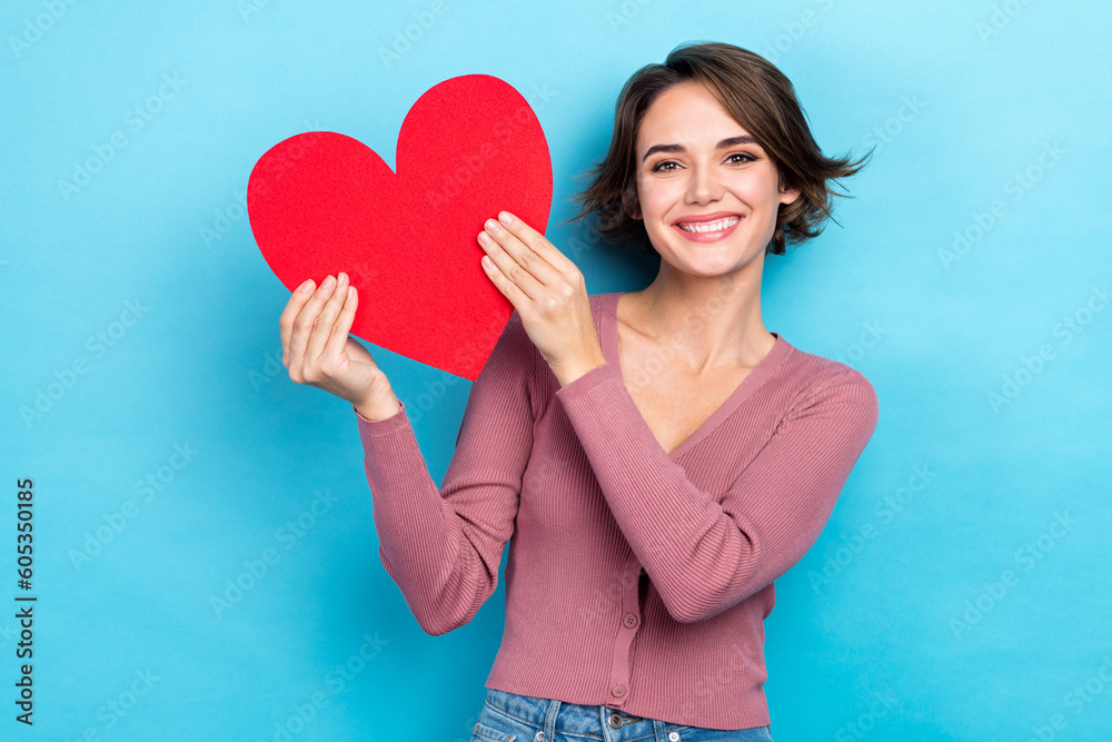 Photo of adorable pretty woman dressed pink shirt smiling rising red heart isolated blue color background Photo of adorable pretty woman dressed pink shirt smiling rising red heart isolated blue color background