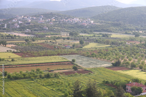 Turkish village, fields and road on the mountain slope on a cloudy day. Agricultural landscape, fields and outbuildings, Mugla, Turkey, May 2023.