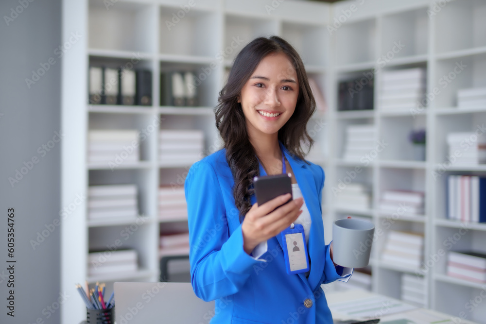 Happy young Asian business woman with a smile using smartphone at the office.