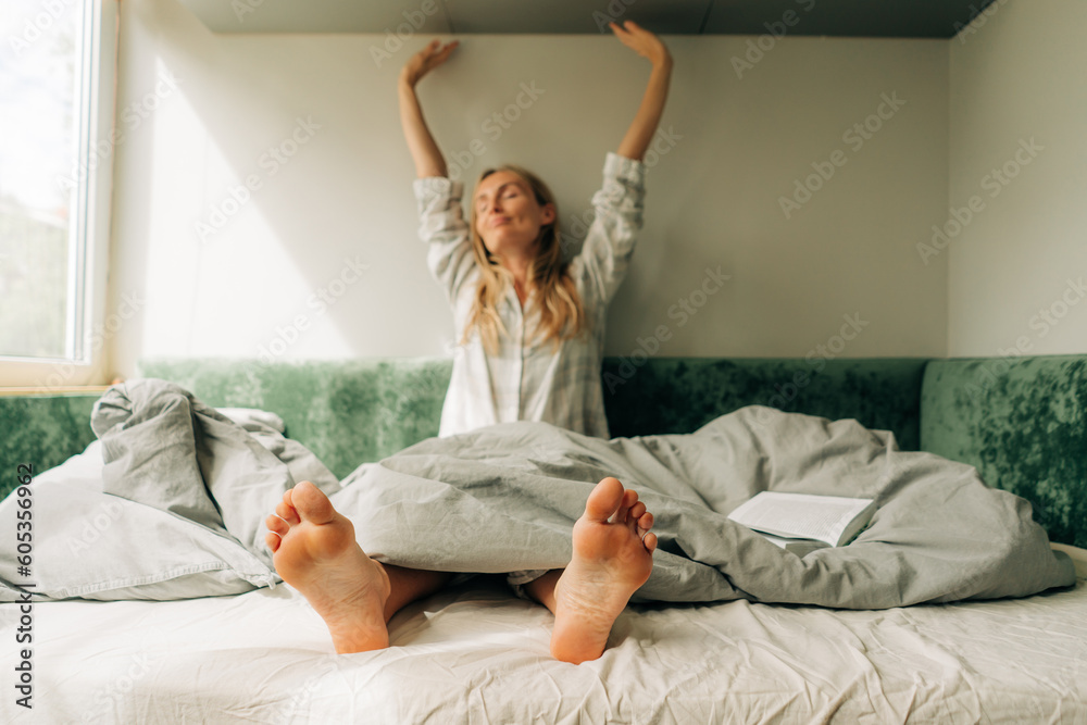 A woman in pajamas stretches after waking up. Blurred portrait of a woman, feet in focus.