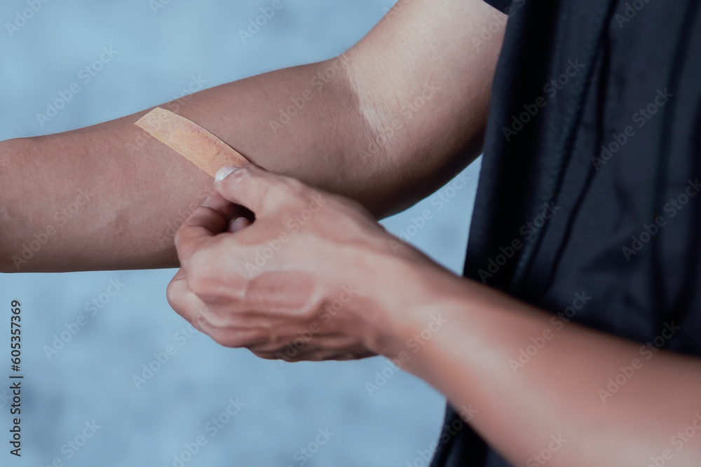 A man putting a plaster on his arm against an abstract light blue background