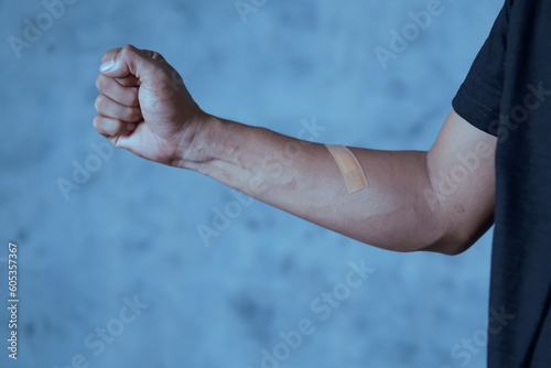 A man putting a plaster on his arm against an abstract light blue background © kanurism