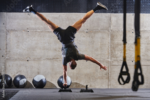 A muscular man in a handstand position, showcasing his exceptional balance and body control while performing a variety of exercises to enhance his overall body stability and strength in a modern gym photo