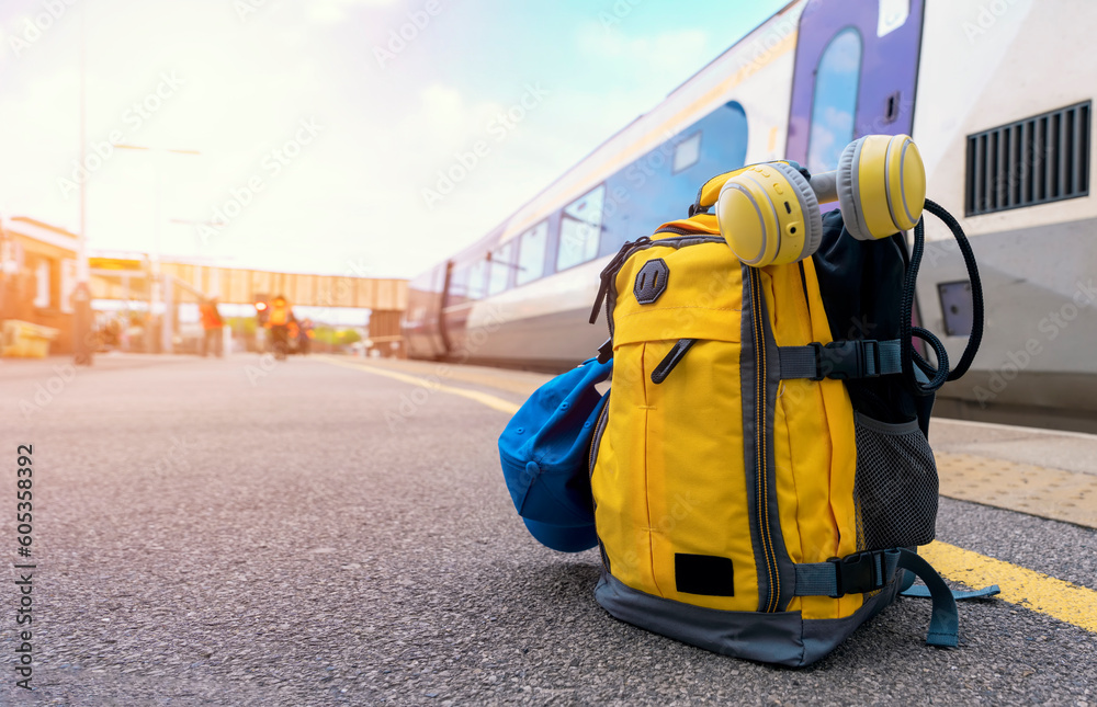 Yellow backpack with headphones and cap on the platform in a train station. Travel touristic concept. travel light