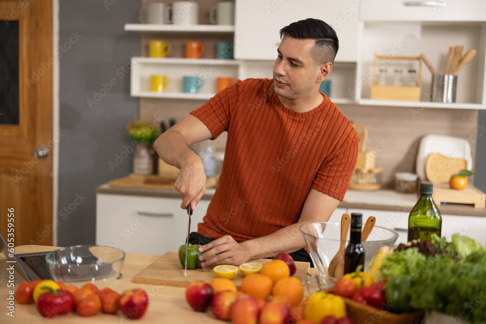 A homely and healthy male prepares nutritious diet, including variety of fruits. Following cooking show on laptop Mastery of peeling, chopping, and slicing fruits to prepare them in artistic style.