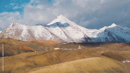 Wide angle shot of Langza Buddha Statue with snow covered Chau Chau Kang Nilda mountain behind it as seen from far away place at Langza in Spiti Valley, Himachal Pradesh, India. Natural background. photo