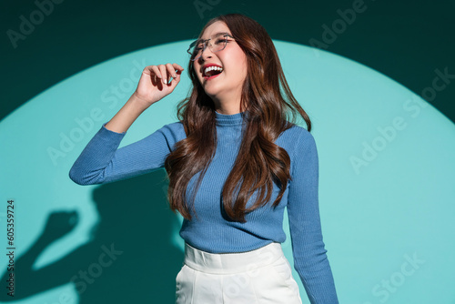 Smiling optimistic Asian casual female woman in blue sweater wear glasses hand playing fun gesture holding her body shape positive thinking portrait shot studio shooting on blue colour background