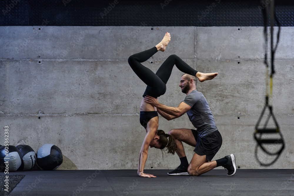 Fototapeta premium A muscular man assisting a fit woman in a modern gym as they engage in various body exercises and muscle stretches, showcasing their dedication to fitness and benefiting from teamwork and support
