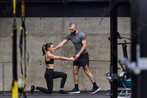 A muscular man assisting a fit woman in a modern gym as they engage in various body exercises and muscle stretches, showcasing their dedication to fitness and benefiting from teamwork and support