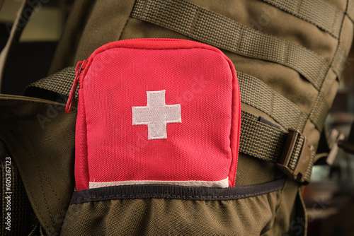 A red first aid kit with a white cross in the pocket of a tactical military olive backpack with a Molle system