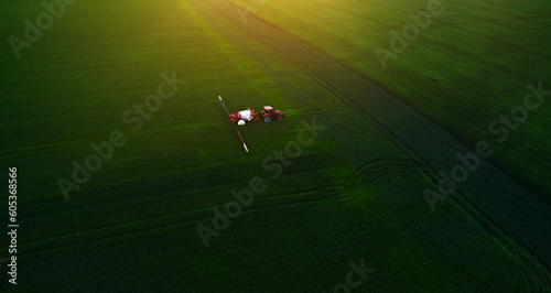 Aerial view of tractor spraying pesticides on wheat field with sprayer in spring.