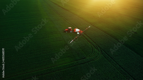 Aerial view of tractor spraying pesticides on wheat field with sprayer in spring.