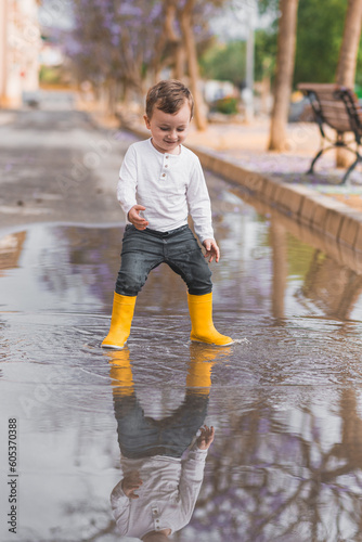 boy in yellow rubber boots jumping over a puddle in the rain © Miri García