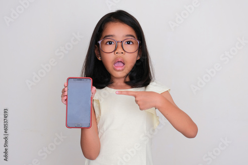Little girl pointing to blank mobile phone screen that she hold with shocked expression photo