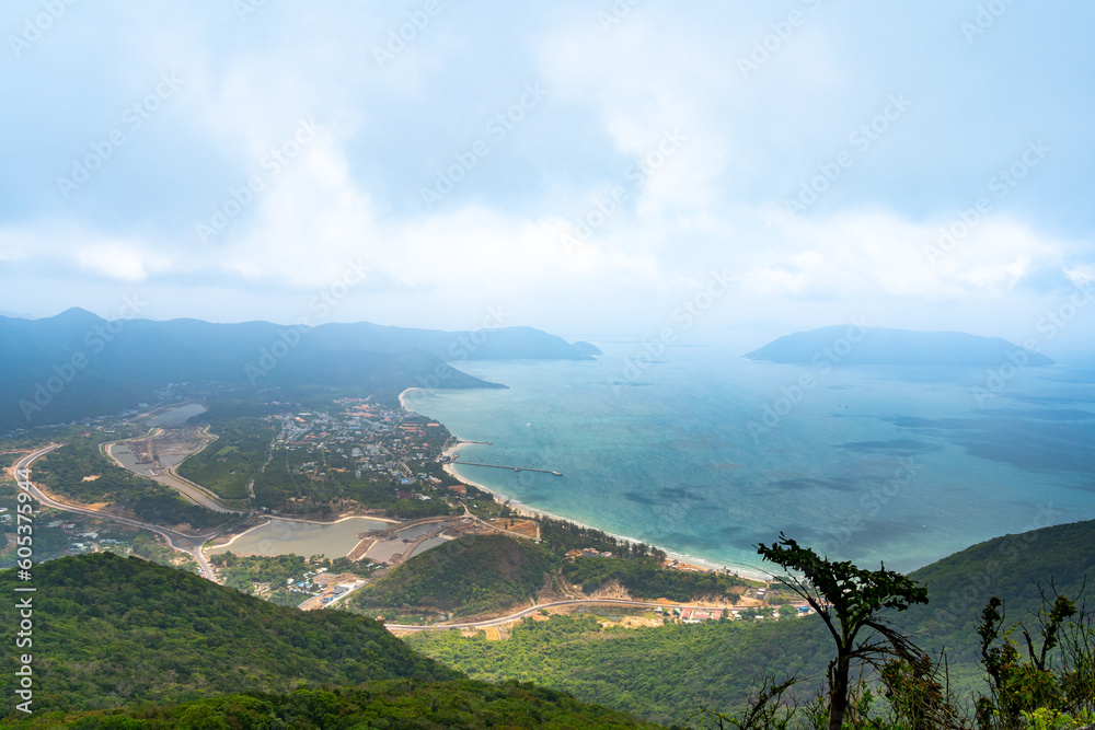 Naklejka premium a peaceful Con Dao island, Vietnam, view from Thanh Gia mountain. Coastal view with waves, coastline, clear sky and road, blue sea and mountain.