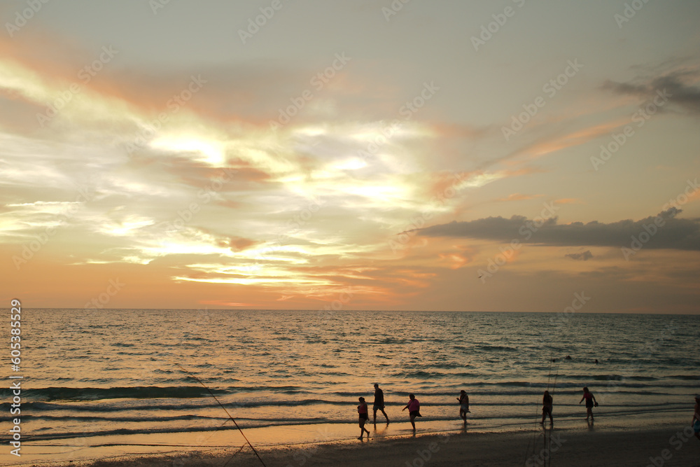 silhouette of people at Florida beach at sunset with blue sky and yellow colors with water and sand. 