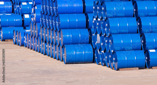Piles of many blue oil drums stacked on industrial yard area in perspective side view